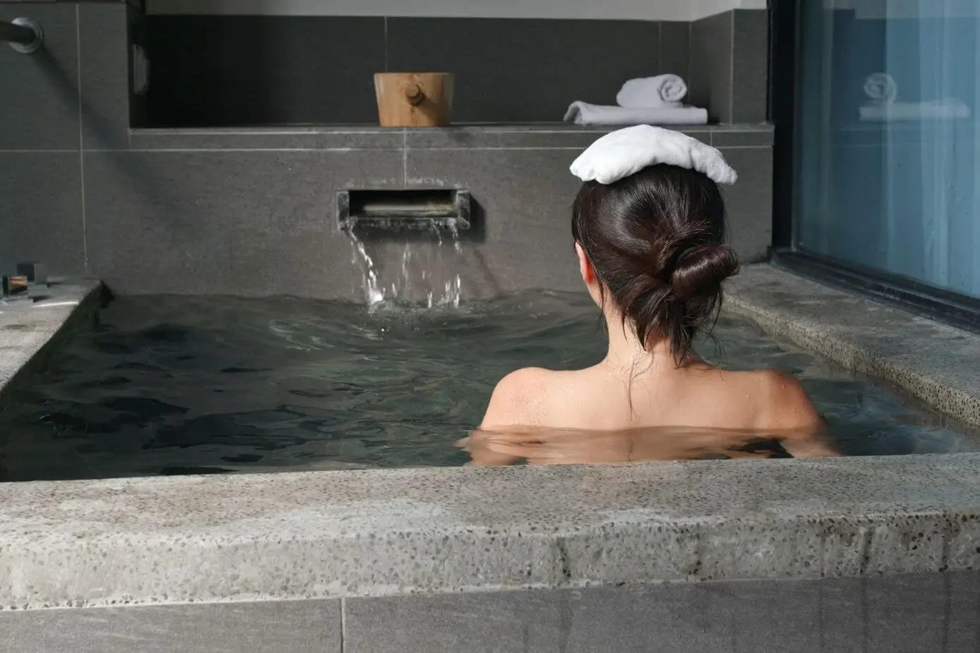 A woman bathing in an onsen with a small towel on her head